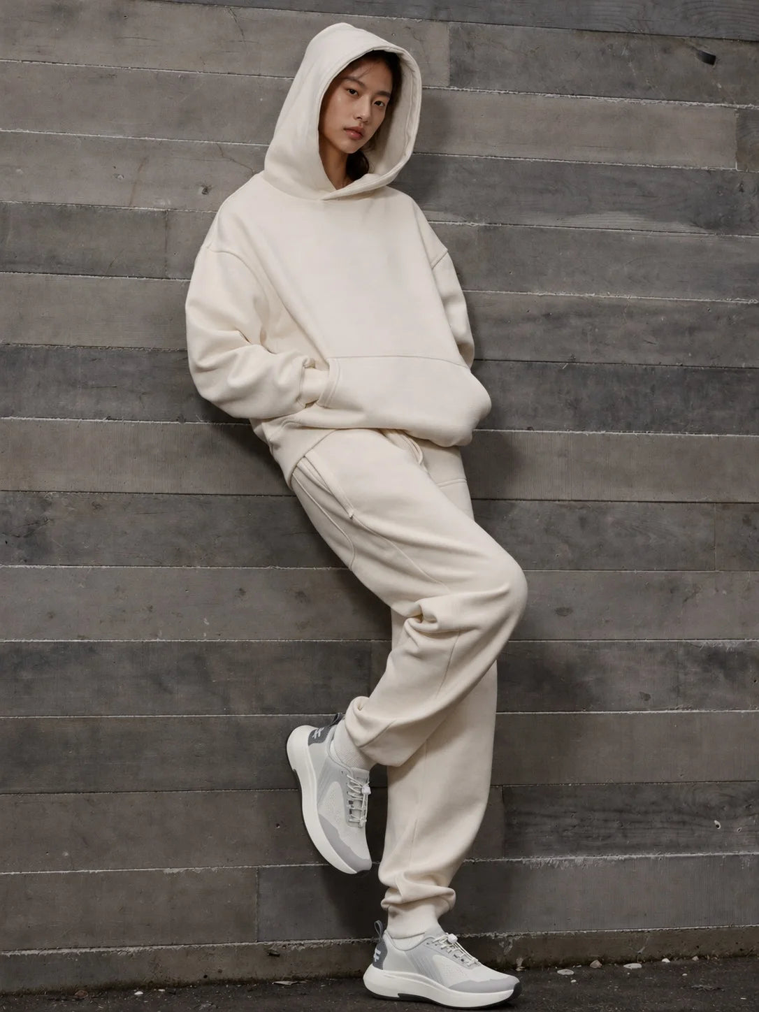 Leaning on a timber wall in a cream hoodie