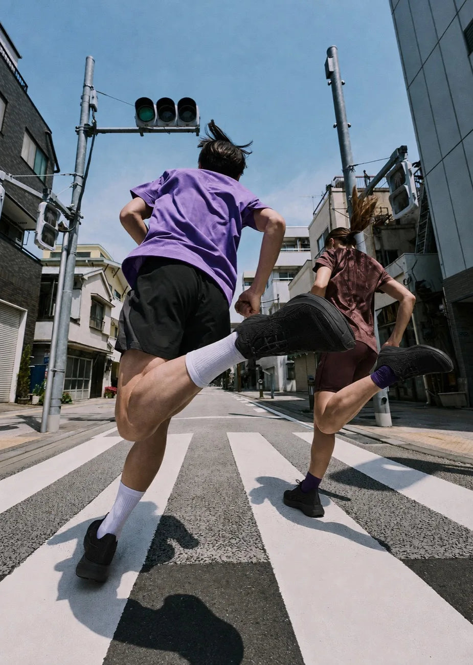 Two runners crossing a city intersection in bright daylight