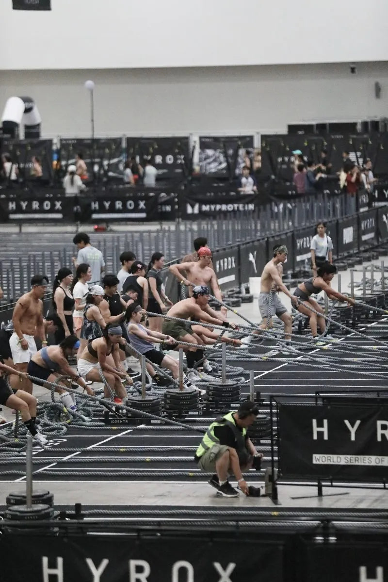 Rows of athletes pulling sled ropes at a HYROX race